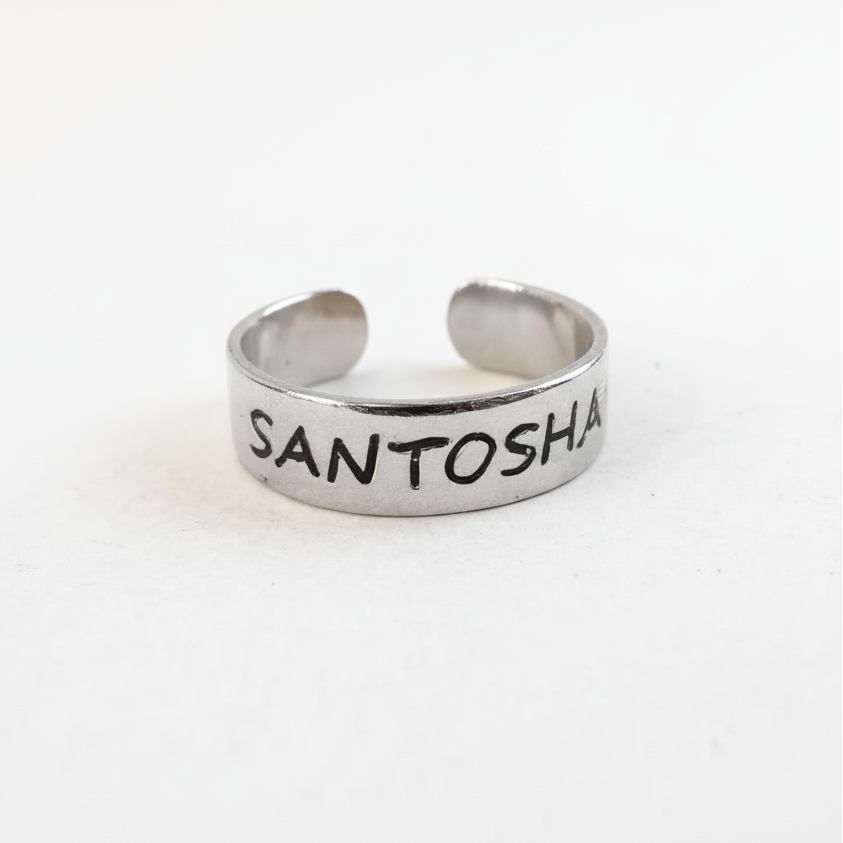 Silver ring with 'SANTOSHA' engraved on a white background